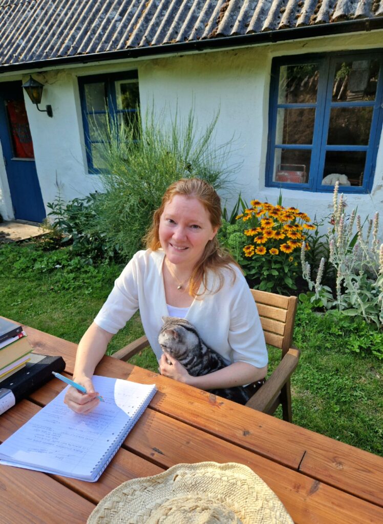 Sara Johansson med katten Jicky (som finns med i boken) redigerar manus till "Förenligt med liv". Foto: Privat. 